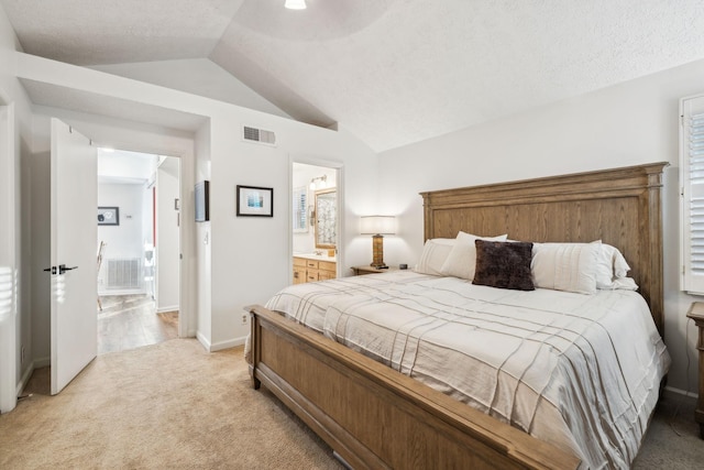 bedroom with vaulted ceiling, light colored carpet, and ensuite bath