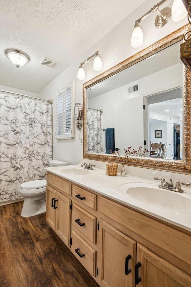 bathroom with vanity, a textured ceiling, hardwood / wood-style floors, toilet, and curtained shower