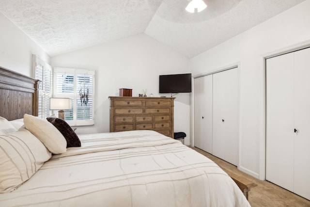 carpeted bedroom with ceiling fan, multiple closets, a textured ceiling, and vaulted ceiling