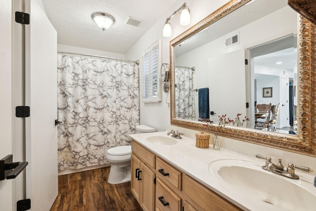 full bathroom featuring hardwood / wood-style floors, vanity, shower / bath combo, toilet, and a textured ceiling