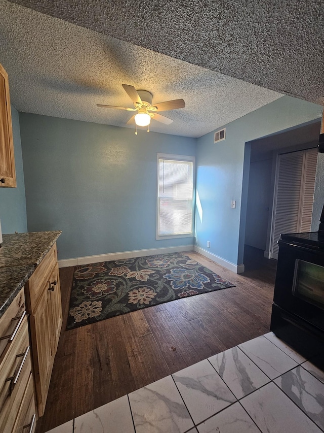 kitchen featuring black range with electric stovetop, ceiling fan, light hardwood / wood-style flooring, dark stone countertops, and a wood stove