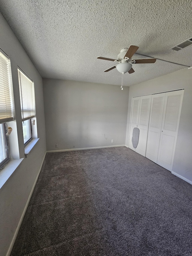 unfurnished bedroom with dark colored carpet, ceiling fan, a textured ceiling, and a closet