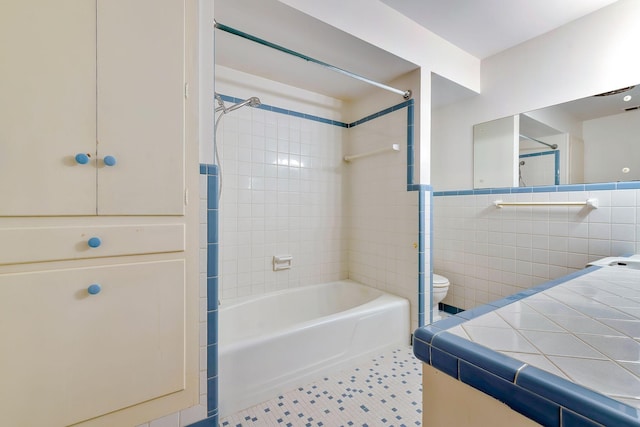 bathroom with toilet, tile walls, and tiled shower / bath