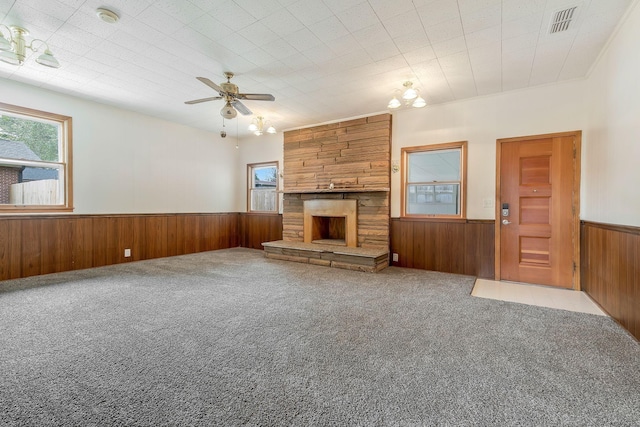 unfurnished living room with carpet, ceiling fan with notable chandelier, a fireplace, and wood walls