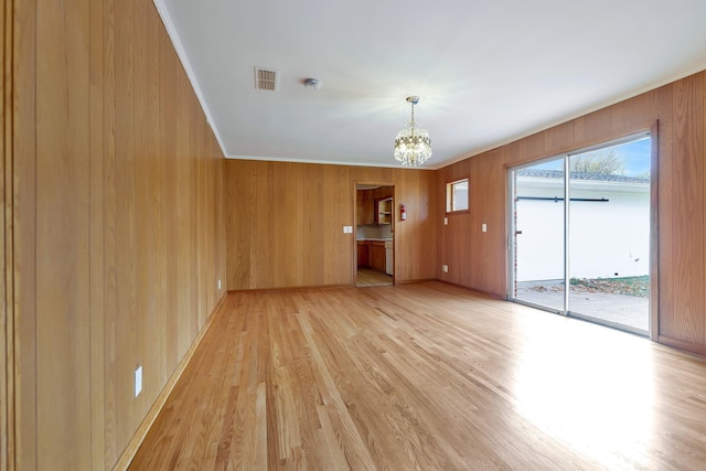 unfurnished living room featuring ornamental molding, wooden walls, light hardwood / wood-style flooring, and a notable chandelier