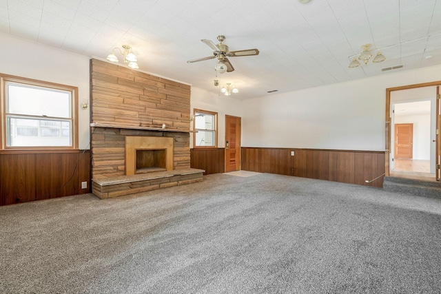 unfurnished living room with carpet flooring, ceiling fan with notable chandelier, and a stone fireplace