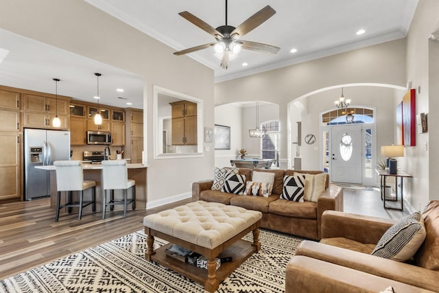 living room with ornamental molding, ceiling fan with notable chandelier, and wood-type flooring