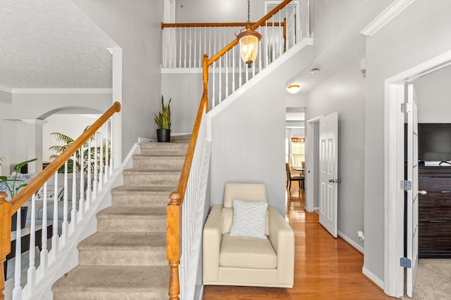 staircase with ornate columns, wood-type flooring, a textured ceiling, and ornamental molding