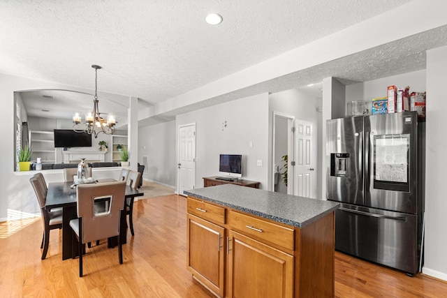 kitchen featuring stainless steel fridge, light wood-type flooring, a chandelier, a kitchen island, and hanging light fixtures