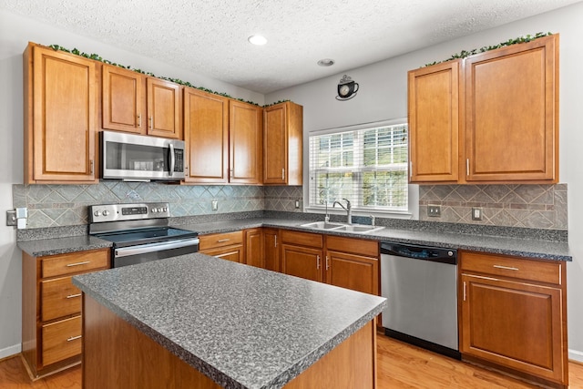 kitchen with sink, light hardwood / wood-style flooring, a textured ceiling, a kitchen island, and appliances with stainless steel finishes