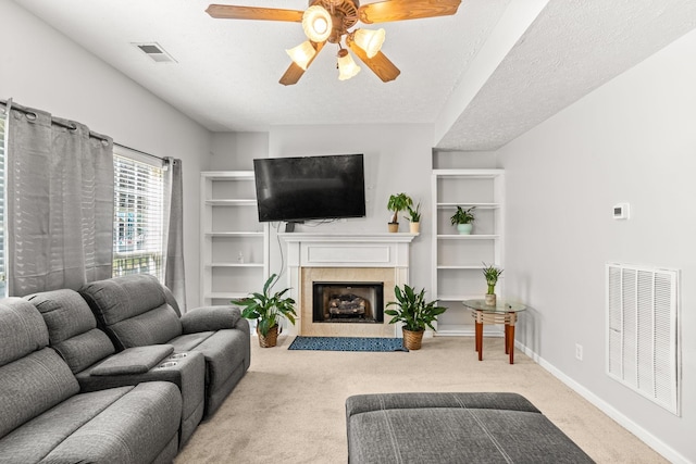 living room featuring light carpet, a fireplace, ceiling fan, and a textured ceiling