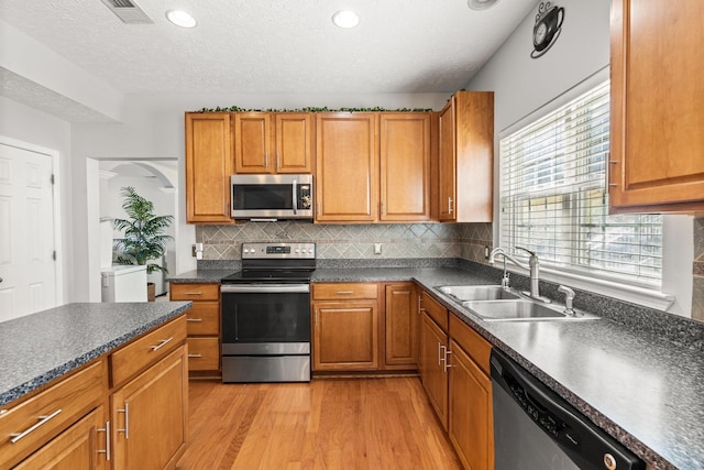 kitchen with tasteful backsplash, a textured ceiling, stainless steel appliances, sink, and light hardwood / wood-style floors