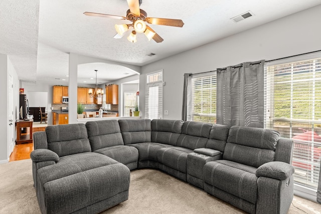 carpeted living room featuring ceiling fan with notable chandelier and a textured ceiling