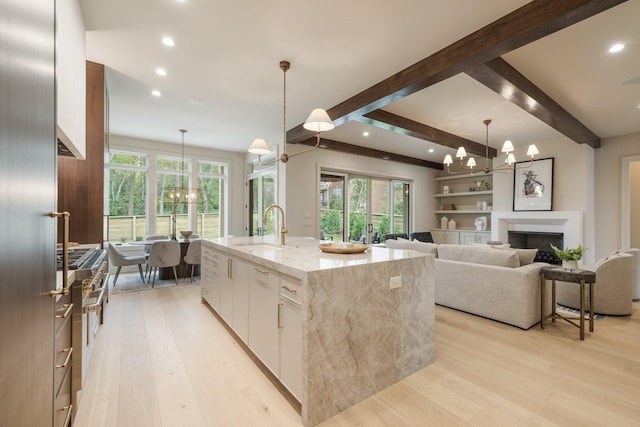 kitchen with light stone countertops, a kitchen island with sink, sink, pendant lighting, and white cabinetry