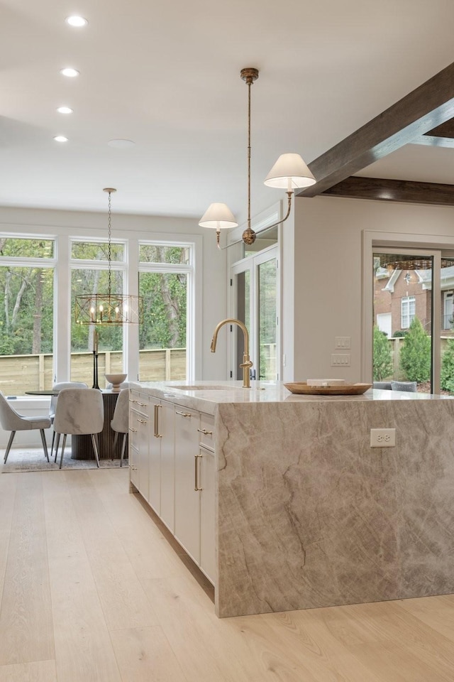 kitchen featuring white cabinetry, hanging light fixtures, light stone counters, light hardwood / wood-style flooring, and beamed ceiling