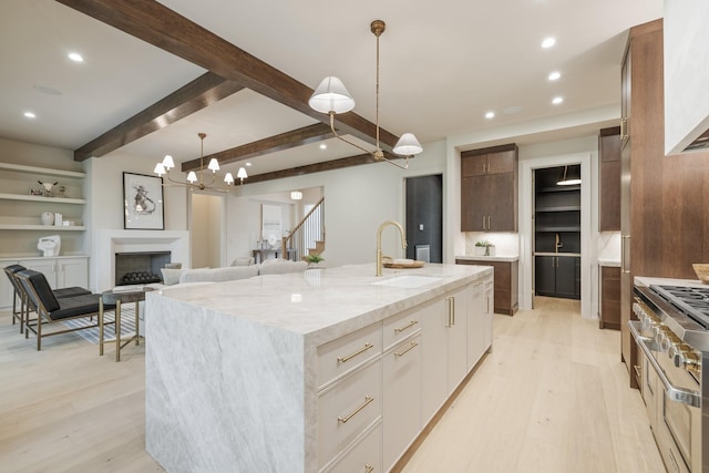 kitchen with white cabinetry, sink, an island with sink, light hardwood / wood-style floors, and decorative light fixtures