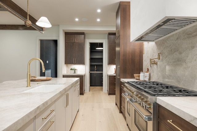 kitchen with range with two ovens, sink, light wood-type flooring, tasteful backsplash, and extractor fan