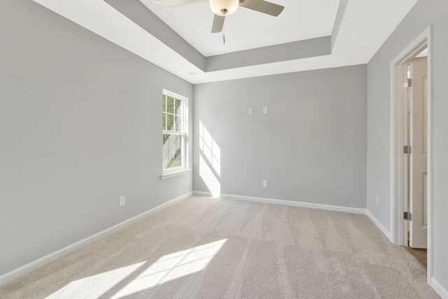 empty room featuring a raised ceiling, ceiling fan, and light colored carpet