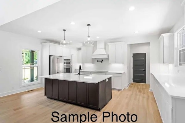 kitchen featuring light wood-type flooring, light countertops, custom range hood, stainless steel appliances, and a sink