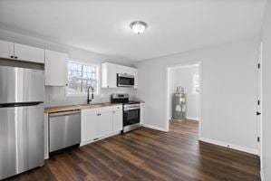 kitchen featuring dark hardwood / wood-style flooring, stainless steel appliances, water heater, sink, and white cabinetry