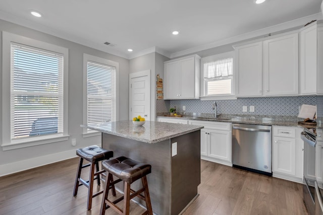 kitchen featuring light stone counters, stainless steel appliances, sink, white cabinets, and a kitchen island