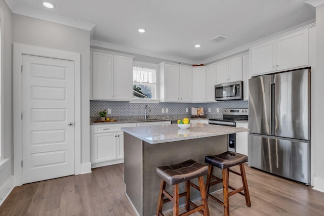 kitchen featuring a breakfast bar, stainless steel appliances, sink, white cabinets, and a center island