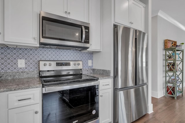 kitchen with white cabinetry, light stone countertops, dark hardwood / wood-style floors, appliances with stainless steel finishes, and ornamental molding