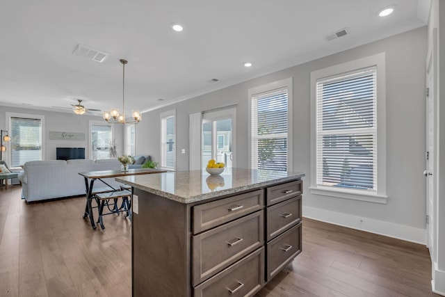 kitchen with a center island, ceiling fan with notable chandelier, dark hardwood / wood-style floors, decorative light fixtures, and light stone counters