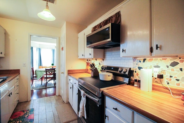 kitchen featuring decorative light fixtures, light hardwood / wood-style flooring, appliances with stainless steel finishes, decorative backsplash, and white cabinets