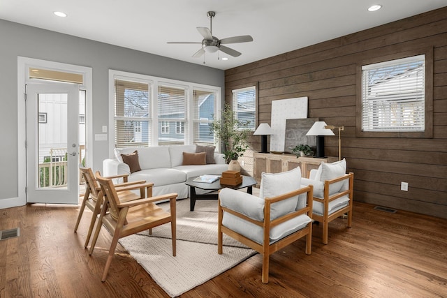 living area with hardwood / wood-style floors, ceiling fan, and wooden walls