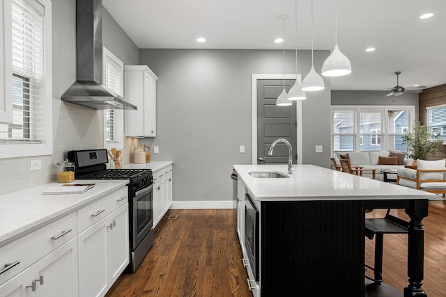 kitchen featuring wall chimney exhaust hood, stainless steel gas range, sink, pendant lighting, and a center island with sink