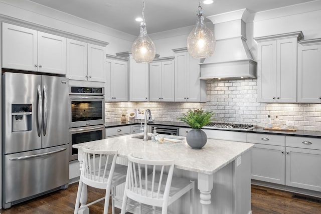 kitchen featuring an island with sink, pendant lighting, a breakfast bar area, appliances with stainless steel finishes, and custom exhaust hood