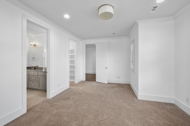 unfurnished bedroom featuring connected bathroom, light carpet, sink, and ornamental molding