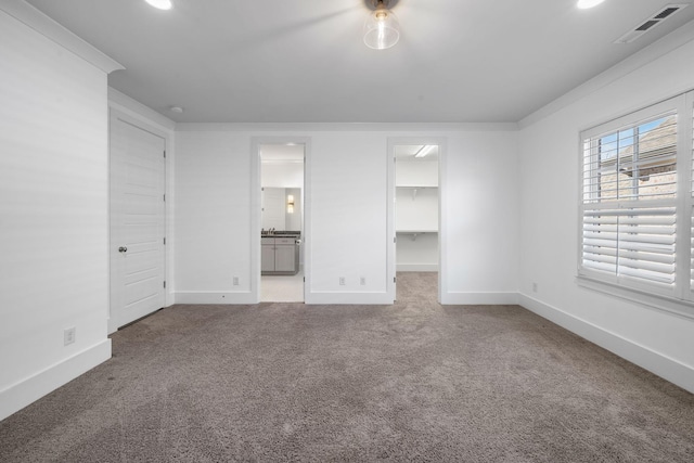 unfurnished bedroom with carpet flooring, a walk in closet, ensuite bath, and a closet