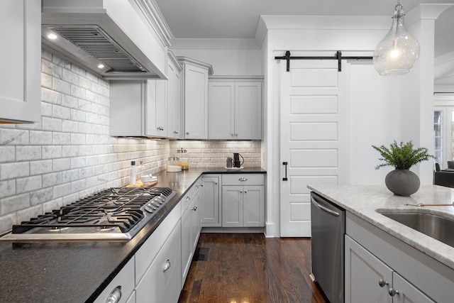 kitchen with custom exhaust hood, a barn door, appliances with stainless steel finishes, tasteful backsplash, and decorative light fixtures