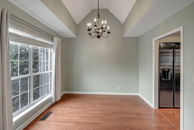 unfurnished dining area featuring a notable chandelier, light hardwood / wood-style flooring, and vaulted ceiling