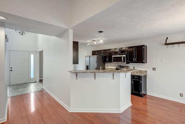 kitchen featuring a breakfast bar, light wood-type flooring, light stone countertops, appliances with stainless steel finishes, and kitchen peninsula