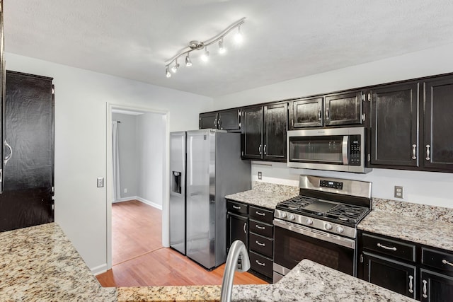 kitchen with light stone countertops, light wood-type flooring, and appliances with stainless steel finishes