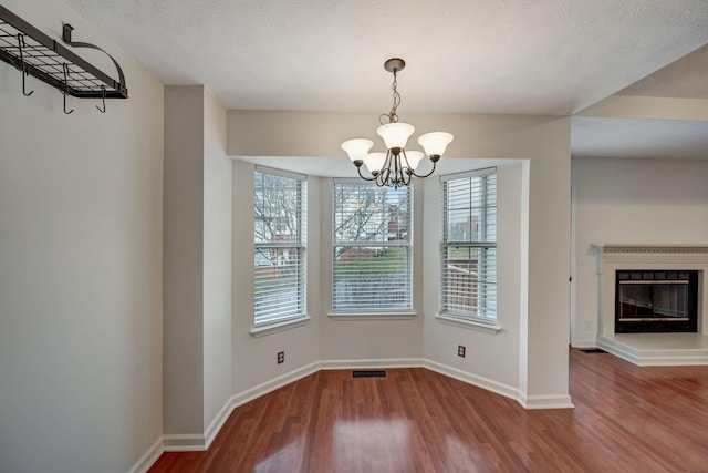 unfurnished dining area with wood-type flooring, a textured ceiling, a wealth of natural light, and a chandelier