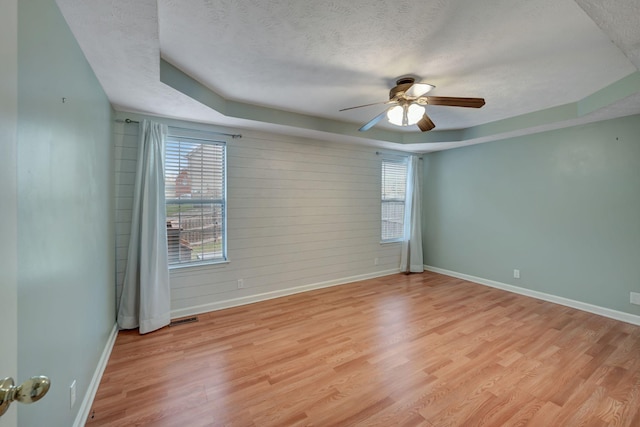 spare room featuring light wood-type flooring, a textured ceiling, a tray ceiling, ceiling fan, and wooden walls