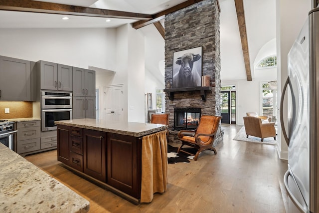 kitchen with a center island, light stone counters, beamed ceiling, a fireplace, and appliances with stainless steel finishes