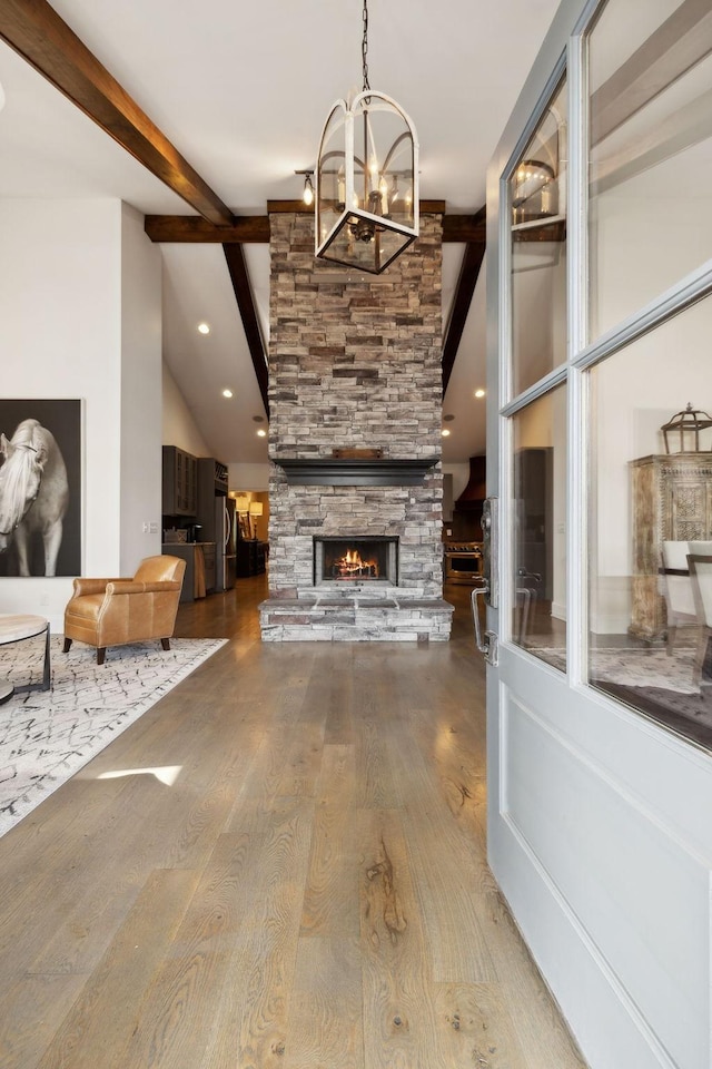 living room with hardwood / wood-style floors, a fireplace, beamed ceiling, and a chandelier