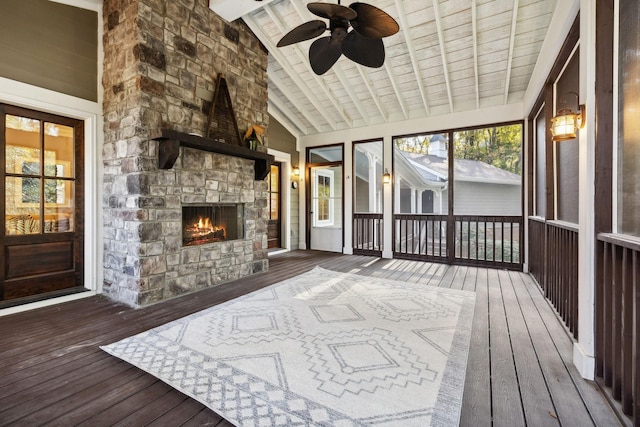 sunroom with lofted ceiling with beams, ceiling fan, and a stone fireplace