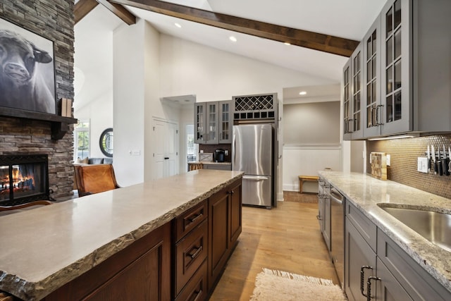 kitchen featuring vaulted ceiling with beams, a stone fireplace, stainless steel appliances, and light hardwood / wood-style flooring