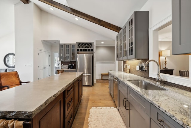 kitchen with sink, light hardwood / wood-style flooring, vaulted ceiling with beams, light stone countertops, and stainless steel appliances