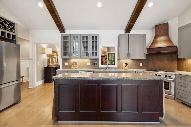 kitchen with appliances with stainless steel finishes, premium range hood, beam ceiling, gray cabinets, and a kitchen island