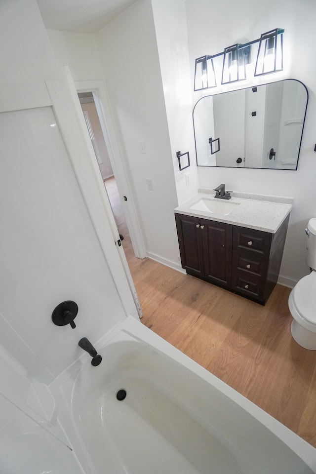 bathroom featuring hardwood / wood-style floors, vanity, a tub to relax in, and toilet