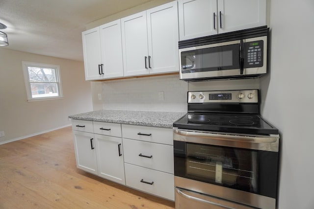 kitchen featuring light stone countertops, backsplash, stainless steel appliances, white cabinets, and light hardwood / wood-style floors