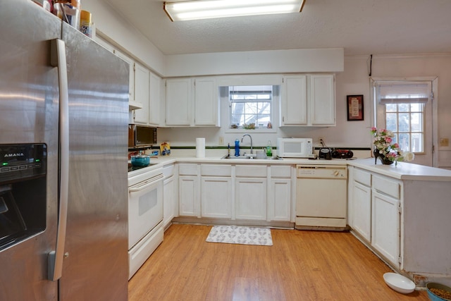 kitchen featuring white appliances, white cabinets, a healthy amount of sunlight, sink, and kitchen peninsula