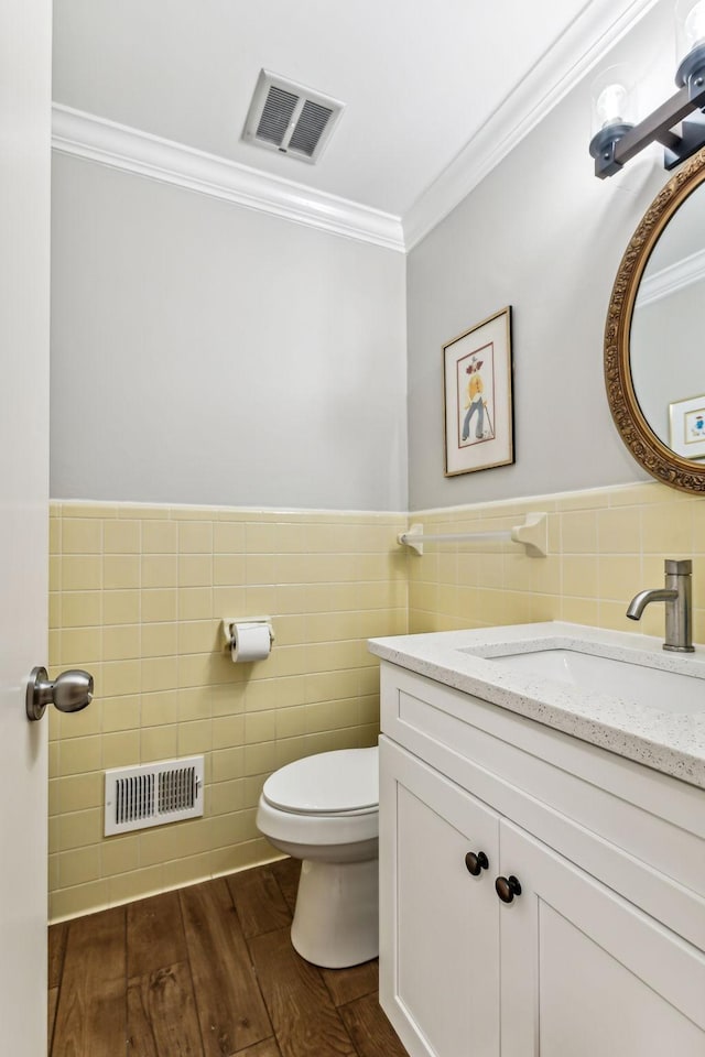 bathroom featuring crown molding, hardwood / wood-style floors, toilet, vanity, and tile walls